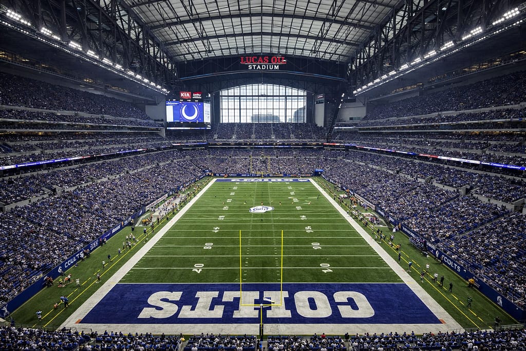 Wide-angle interior view of Lucas Oil Stadium in Indianapolis during an NFL game, showing the full football field, Colts end zones, retractable roof structure, packed stands, and stadium architecture.